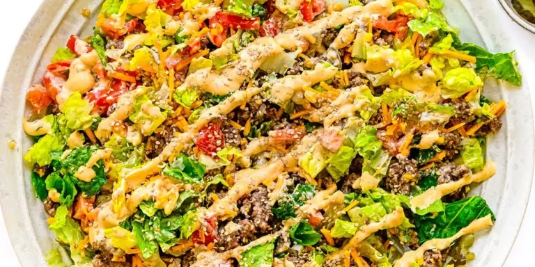 Low-carb Big Mac salad recipe in a bowl with ground beef, special sauce, cheese, pickles, and sesame seeds on a wood table