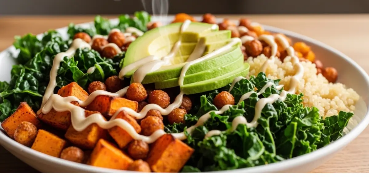 Vegan comfort food bowl recipe with roasted sweet potatoes, chickpeas, quinoa, kale, avocado, and tahini sauce on a rustic wooden table