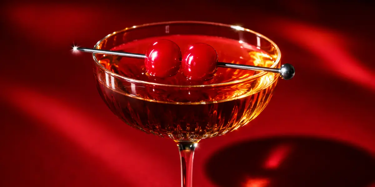 Classic manhattan drink recipe served in a coupe glass with a cherry garnish on a dark bar